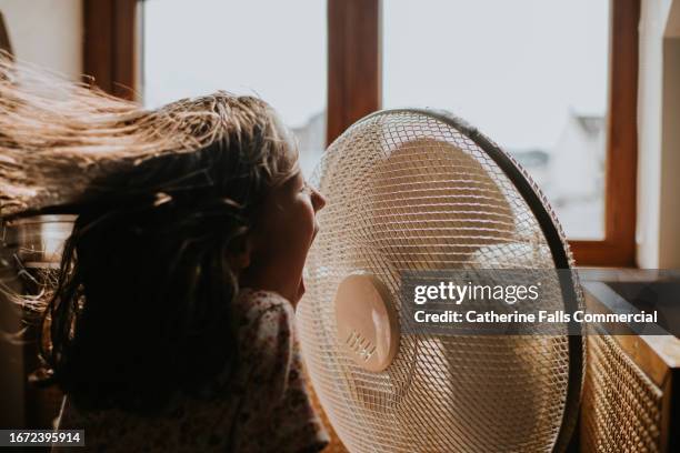 a little girl enjoys cool air blowing in her face from an old fashioned large desk fan. - cooling down stockfoto's en -beelden