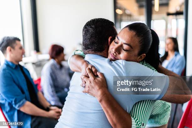 pareja madura abrazada después de hablar en una terapia grupal en un centro de salud mental - desintoxicación fotografías e imágenes de stock