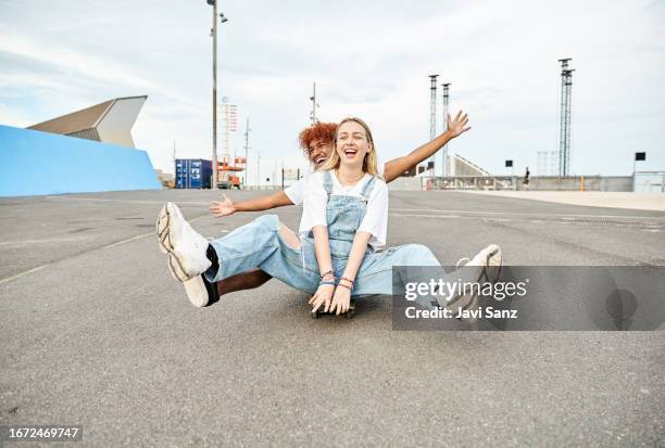 angled view of two teenage hipster friends having fun skateboarding down the road. - roll call stock pictures, royalty-free photos & images