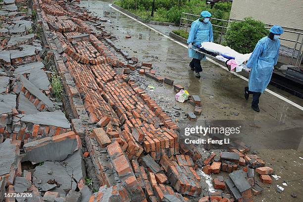 Two security guards carry the dead body of a victims through the ruins at a hospital on April 23, 2013 in Lushan county of Ya An, China. A magnitude...