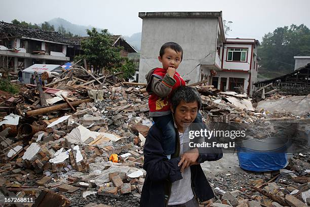 An old man and his grandson walk past the ruins of their house on April 23, 2013 in Longmen township of Lushan county, China. A magnitude 7...