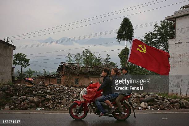 Earthquake survivors carry the flag of the Communist Party of China and ride a motorcycle past a collapsed building after a strong earthquake hit...