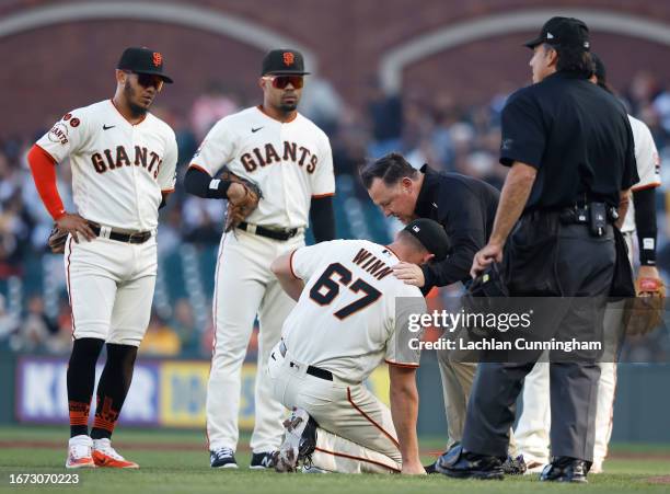 Pitcher Keaton Winn of the San Francisco Giants is assisted by trainer Dave Groeschner after being hit by a ground ball by Elehuris Montero of the...