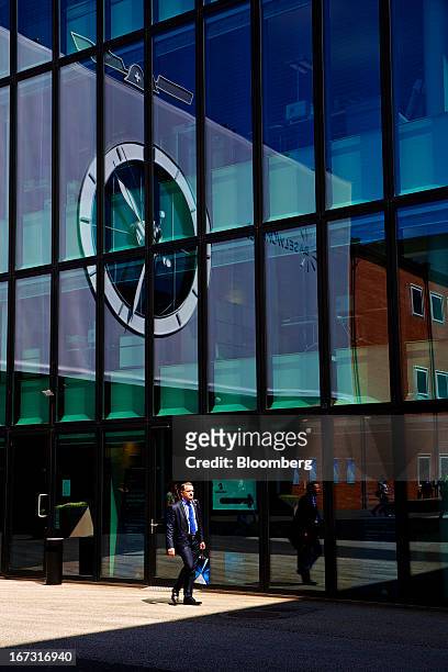 Visitor passes a reflection of a giant watch face outside the Baselworld watch fair in Basel, Switzerland, on Wednesday, April 24, 2013. The annual...