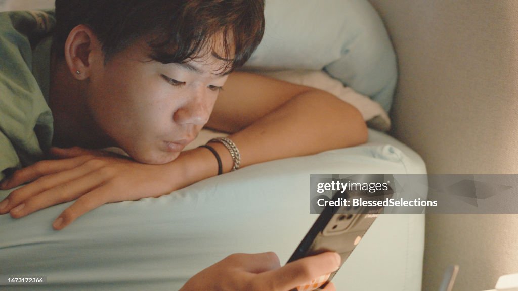 Mixed Asian teenage boy lying on bed with smartphone