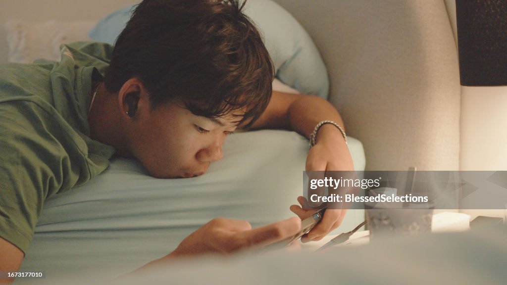 Mixed Asian teenage boy lying on bed with smartphone