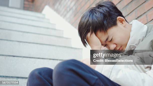depressed mixed asian teenage boy sitting on staircase - low self esteem stock pictures, royalty-free photos & images