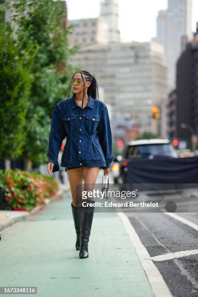 Guest wears a blue denim jacket worn as a mini dress, a mini skirt, dark green knee high boots, a bag, outside Ndigo, during New York Fashion Week,...
