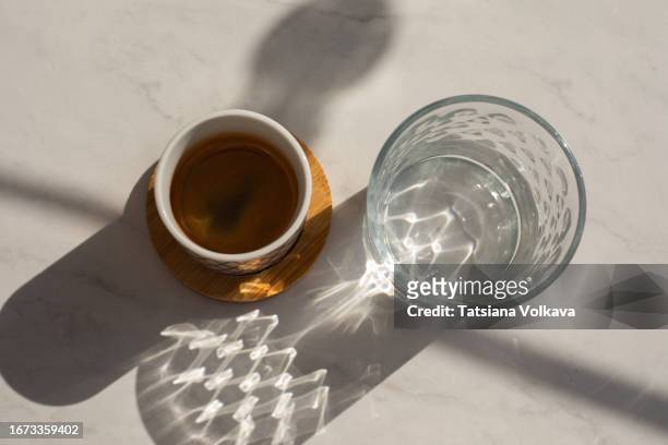 view from above of minimalistic tableau created with cup of black coffee standing on coaster and glass of water, placed on clean table. - coaster stock pictures, royalty-free photos & images