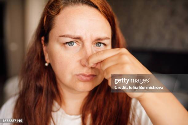 photo of attractive redhead lady standing in bedroom with fingers pinching nose displaying heightened smell sensitivity - long nose ストックフォトと画像