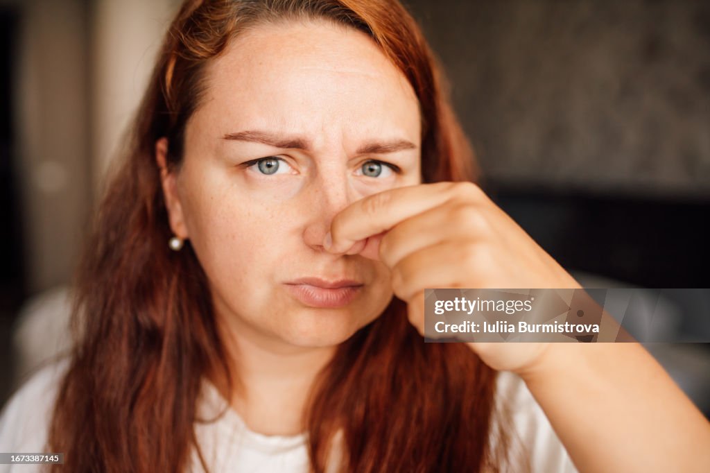 Photo of attractive redhead lady standing in bedroom with fingers pinching nose displaying heightened smell sensitivity
