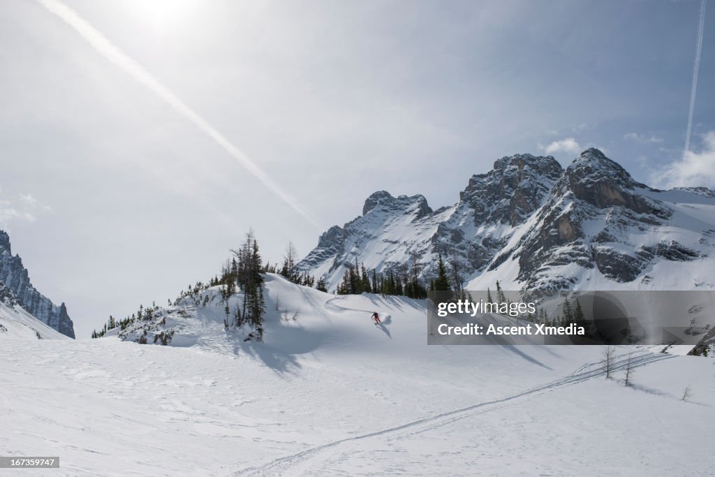 Distant skier descends snowy hillside above path