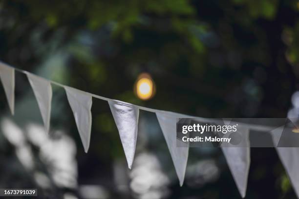 close-up of white flag garland against trees and fairy lights. garden party, summer festival, birthday party, baptism or wedding. - baptism party stock pictures, royalty-free photos & images