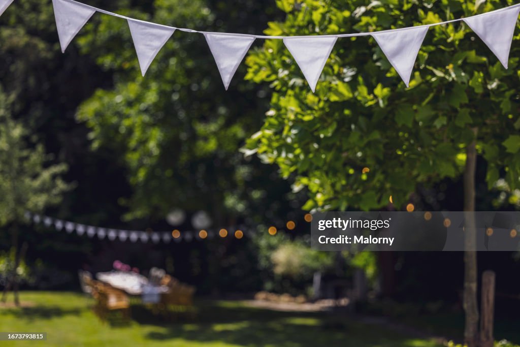 Decorated garden with set table, flag garland and paper lanterns. Garden party, summer festival, birthday party, baptism or wedding.