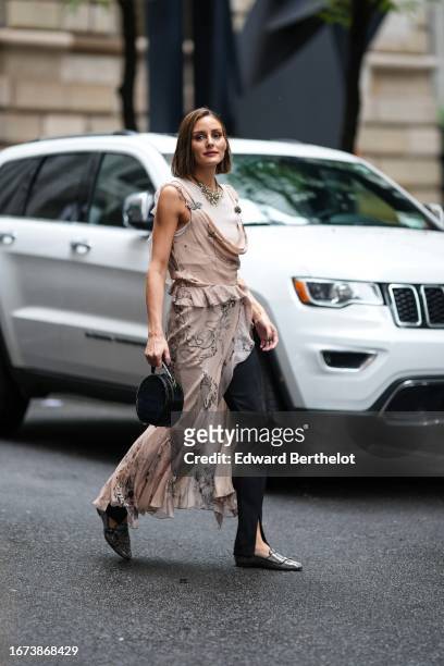Olivia Palermo wears a silver large necklace, a sleeveless ruffled slit flowing dress with floral print, black slit pants, a leather bag, shiny...