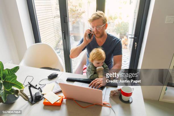 shot of a mature red headed man working from home with his baby daughter on his lap - father baby stock pictures, royalty-free photos & images