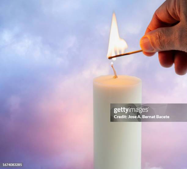 a man's hand lights a candle outdoors at sunset, preparing a romantic candlelight dinner. - vela equipamento de iluminação imagens e fotografias de stock