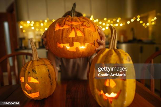 cute little boy playing with scary jack o' lantern pumpkin decoration at home in the evening - jack o' lantern 個照片及圖片檔