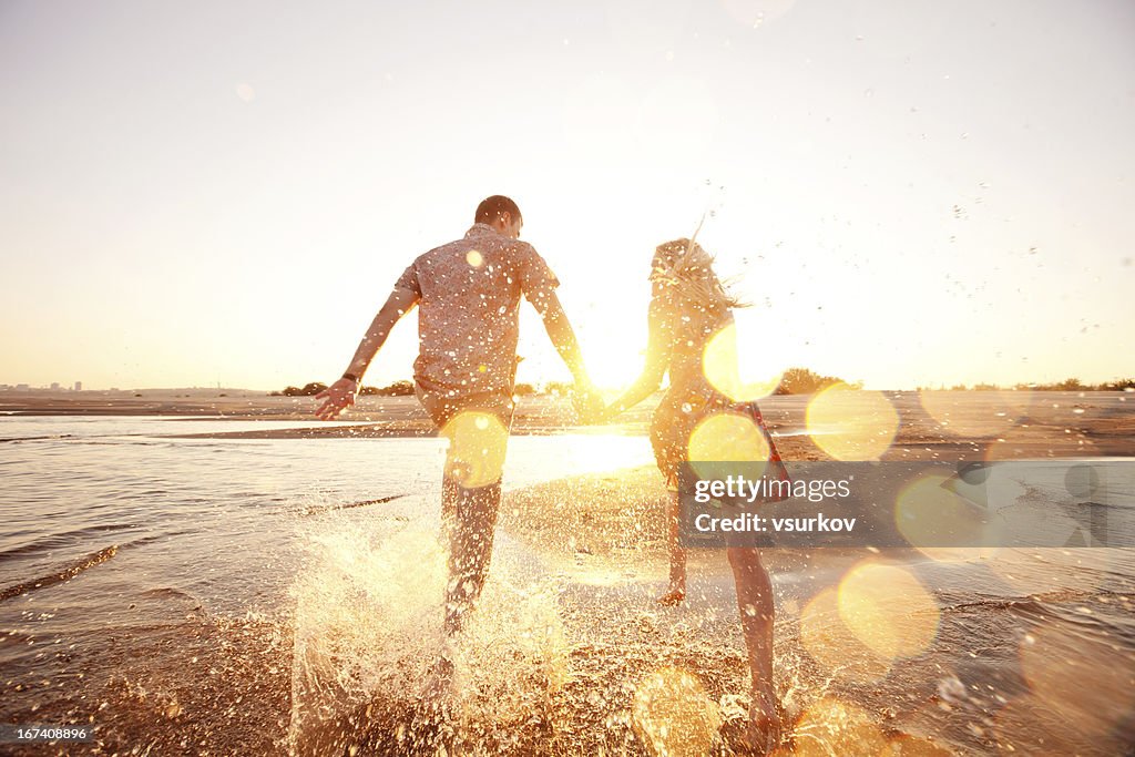 A happy couple runs through waves on sunlit beach