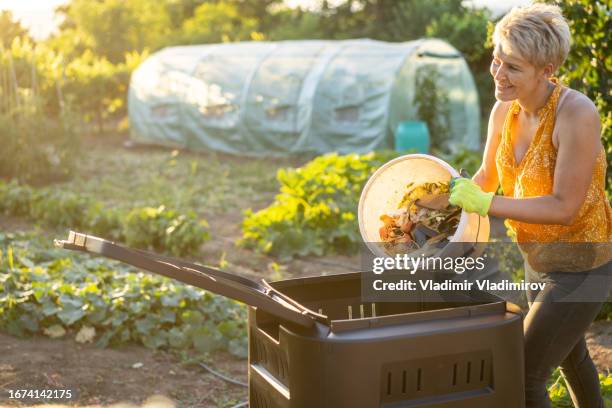 una mujer vaciando los residuos de comida en un compostador de jardín en casa - jardinería orgánica fotografías e imágenes de stock