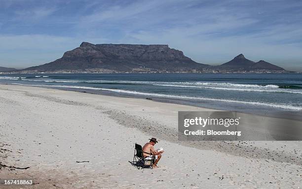 Tourist sits and reads at the seaside on Table Bay beach with a view of Table Mountain, center, in Cape Town, South Africa, on Wednesday, April 24,...