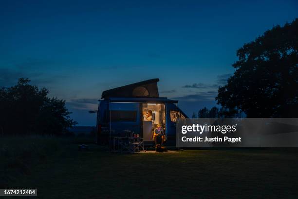 a wide dusk shot of a family with their young baby in their campervan - van life - lieferwagen stock-fotos und bilder
