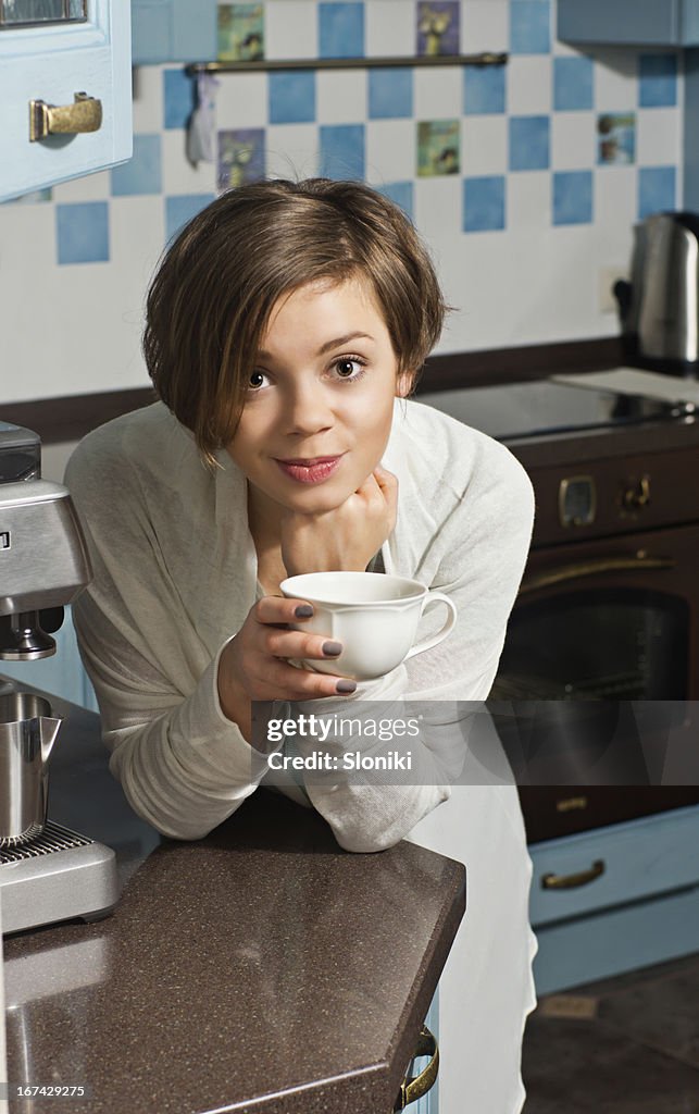 Mujer joven en mostrador de cocina sosteniendo taza de té