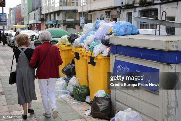 Two women walk next to overflowing garbage containers during the fourth week of the Vilalba garbage collection strike on September 11 in Vilalba,...