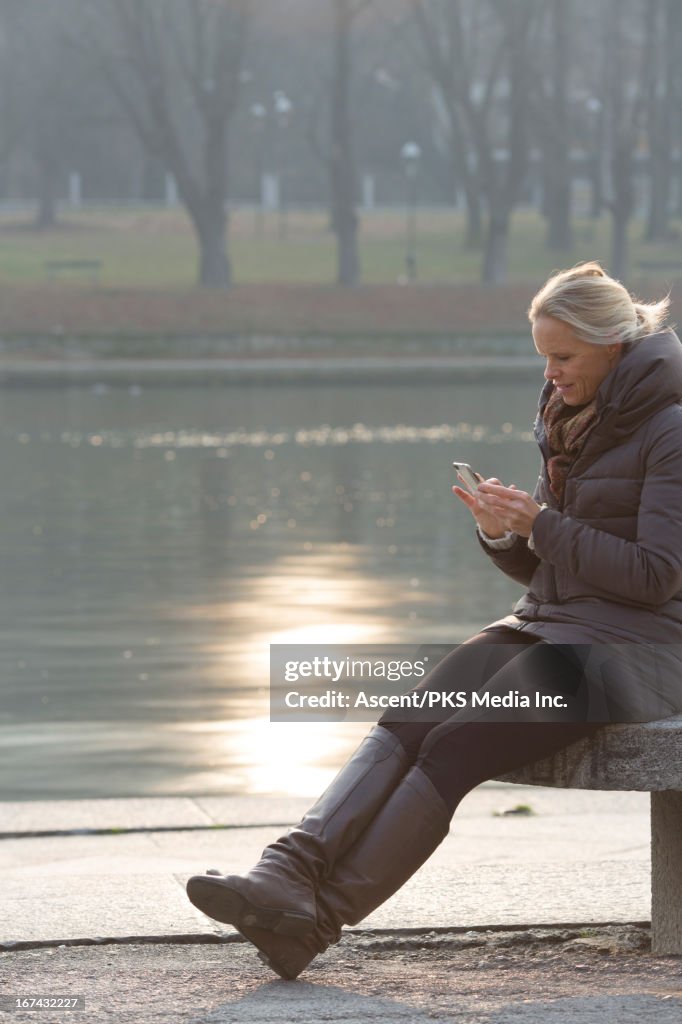 Woman sending text from bench by river's edge