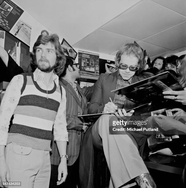 English singer Elton John signing copies of his new album, 'Don't Shoot Me I'm Only the Piano Player', at the Record Bar, a shop owned by radio...