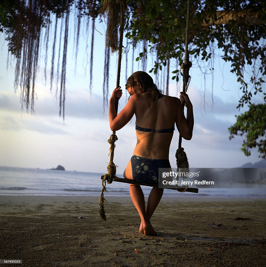 A tourist sits in a wooden swing hanging from a tree...