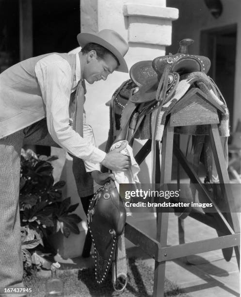 American actor Gary Cooper maintains his saddle. About 1930. Photograph. Der US-amerikanische Schauspieler Gary Cooperpflegt sein Sattelzeug. Um...