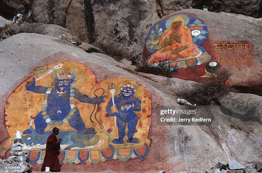 A monk walks past large painted rock carvings on the...