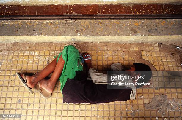 With his bag of glue wrapped tightly in his hand, a teenage street kid lies passed out on a sidewalk with a glue high. He is part of about 20 kids...