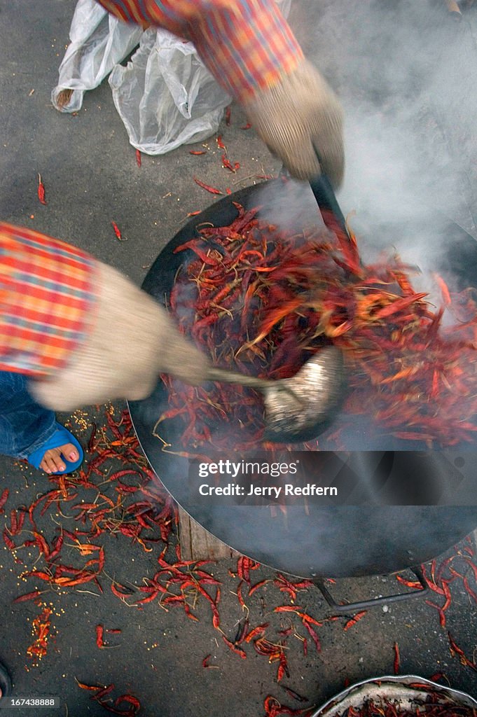 A woman sears chilies in a wok over a coal fire at the...