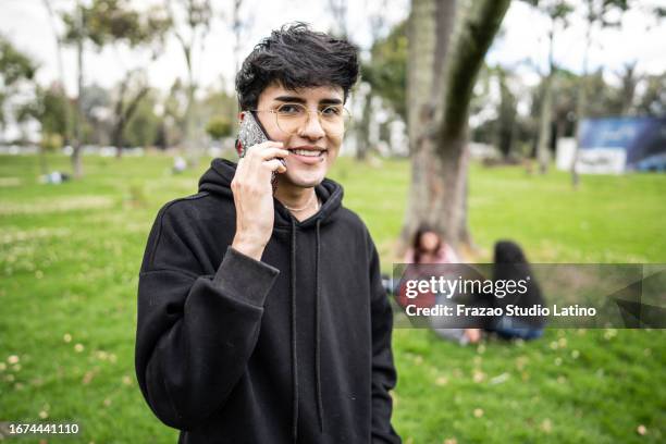 ritratto di un giovane che parla al telefono cellulare nel parco pubblico - capelli neri foto e immagini stock