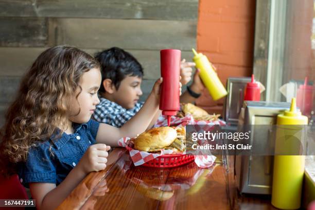 mixed race children having burgers in restaurant - children restaurant stockfoto's en -beelden