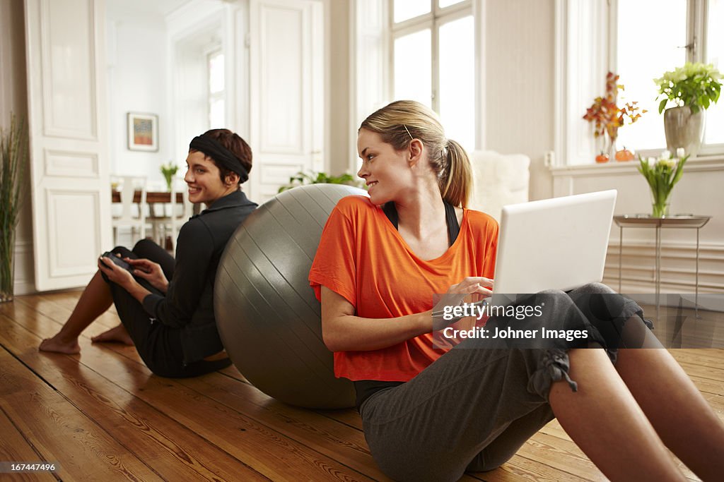 Two women sitting on floor leaning on fitness ball