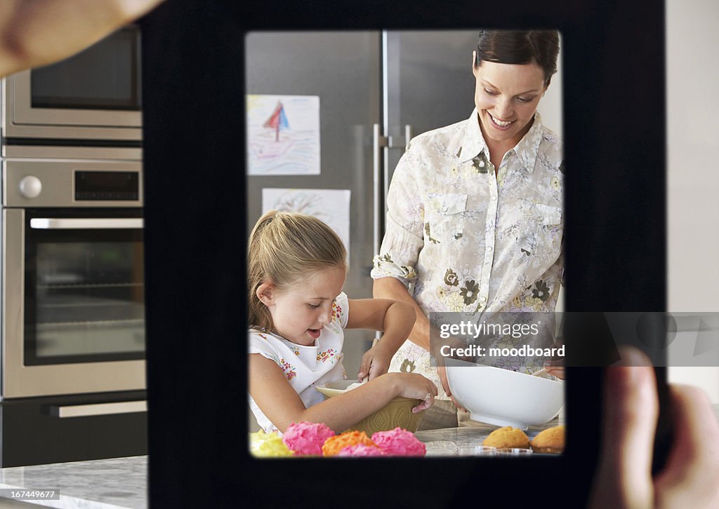 Female hand framing mother and daughter baking together in kitchen