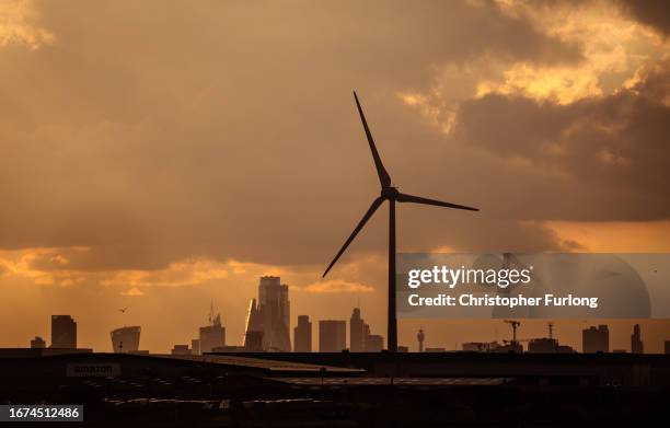 The sun sets behind a wind turbine, Canary Wharf and London on September 11, 2023 in Dagenham, United Kingdom.