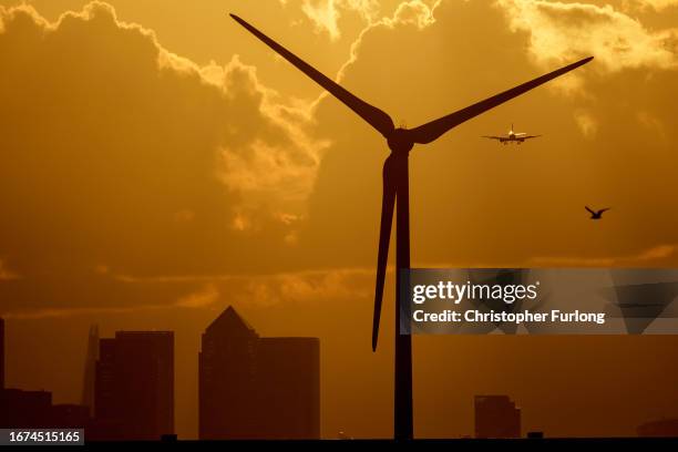 An aircraft comes in to land at London City Airport as the sun sets behind a wind turbine, Canary Wharf and London on September 11, 2023 in Dagenham,...