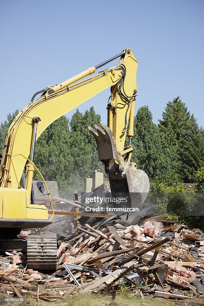 A bulldozer demolishing something wooden on clear blue day.