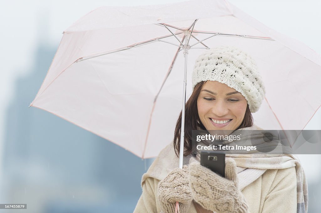 USA, New Jersey, Jersey City, Woman with umbrella using phone