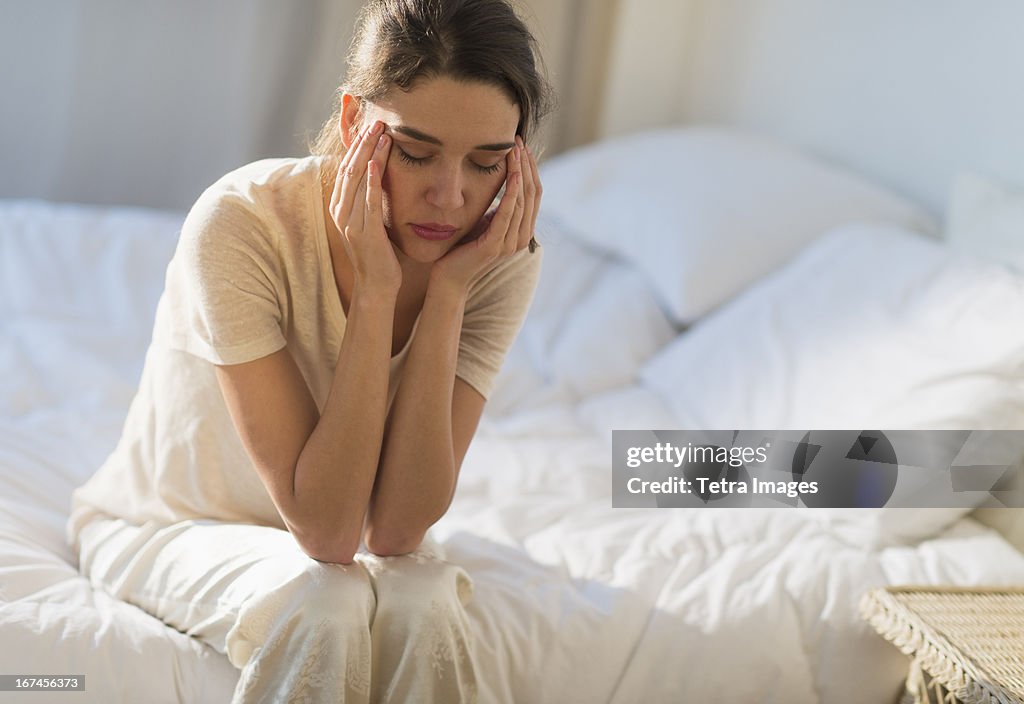 USA, New Jersey, Jersey City, Young woman sitting on bed with headache