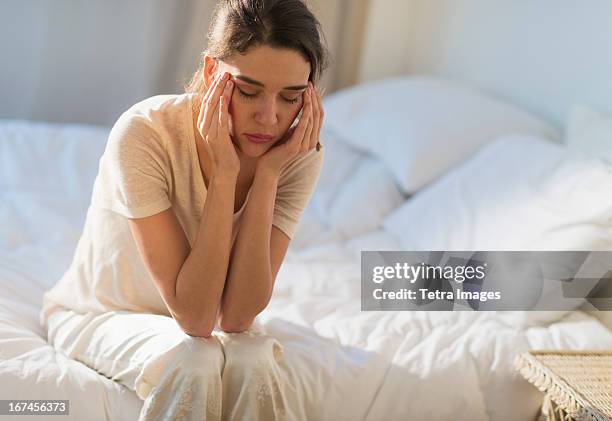 usa, new jersey, jersey city, young woman sitting on bed with headache - headache imagens e fotografias de stock