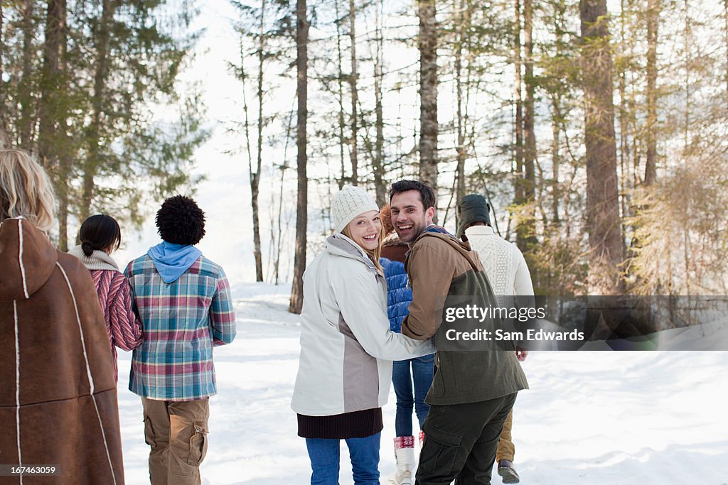 Portrait of smiling couple holding hands and walking with friends in snowy woods