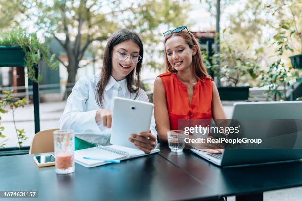 zwei junge freundinnen, die sich ein video auf einem tablet ansehen, während sie in einem café sitzen - university students real studying stock-fotos und bilder