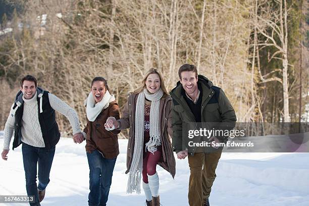 portrait of smiling friends holding hands and running in snow - sam field stockfoto's en -beelden