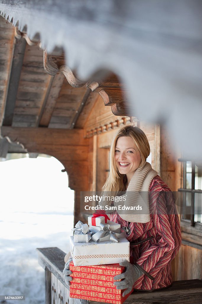 Portrait of smiling woman holding Christmas gifts on cabin porch