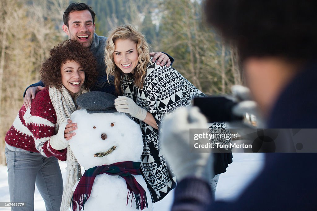 Man photographing friends with snowman